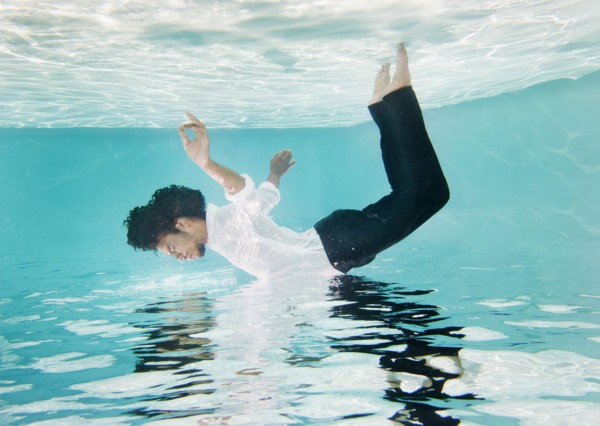 Mixed race man in clothes underwater in swimming pool