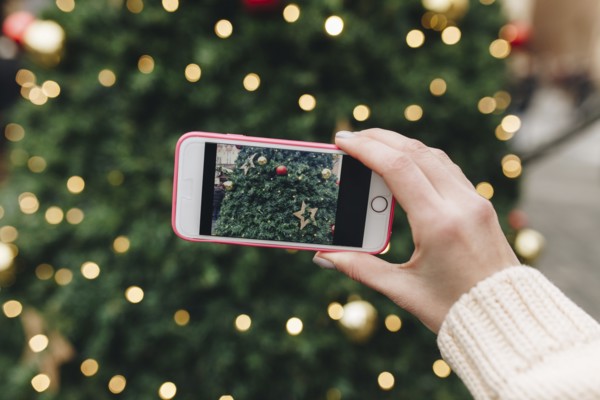 Hand of Caucasian woman photographing Christmas tree with cell phone
