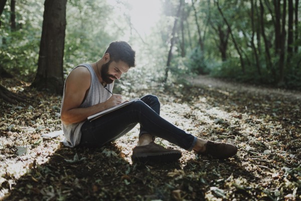 Caucasian man sitting in woods drawing on sketchpad