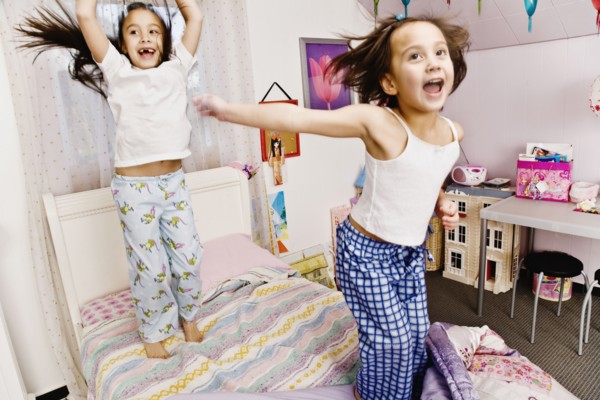 Asian sisters jumping on bed
