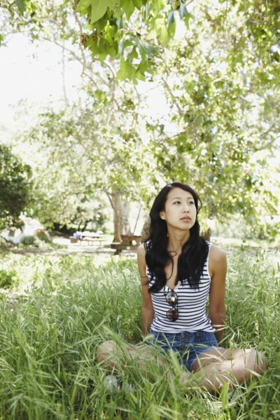 Asian woman sitting cross-legged in grass