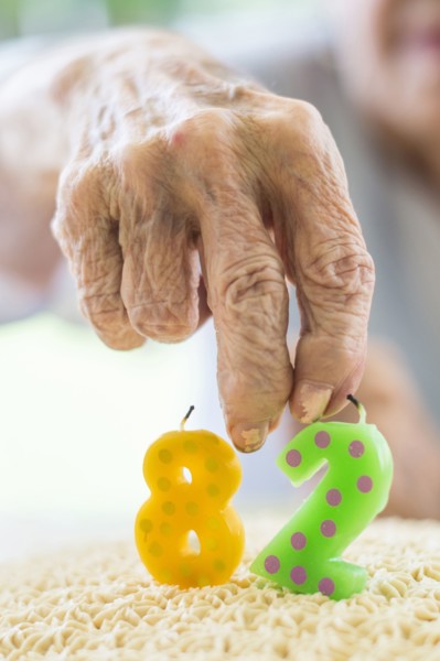Close up of wrinkled hand holding birthday cake candle