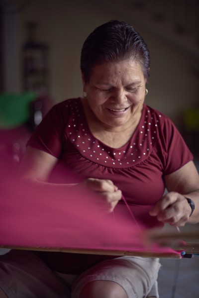 Hispanic woman weaving fabric on loom