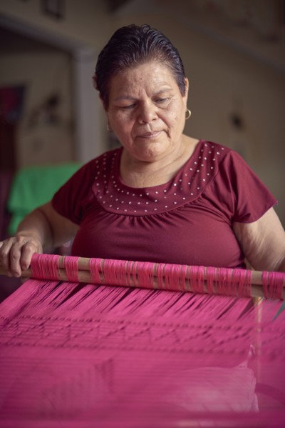 Hispanic woman weaving fabric on loom