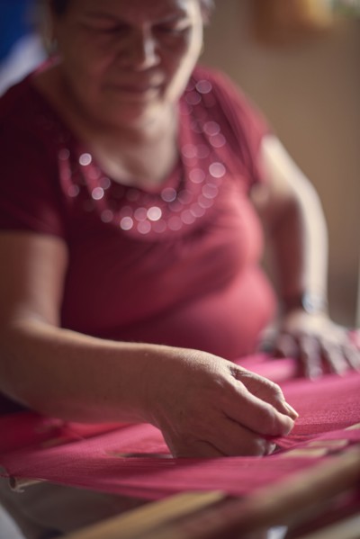 Hispanic woman weaving fabric on loom