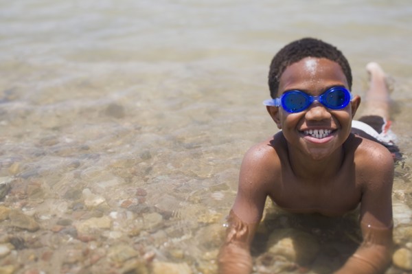 African boy wearing goggles and laying in shallow lake