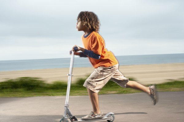 Mixed Race boy riding foot-powered scooter