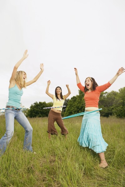 Three young women playing with plastic hoops in meadow