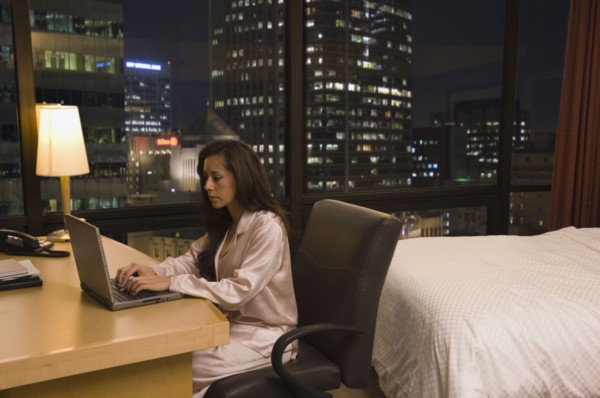 Hispanic woman typing on laptop in hotel room