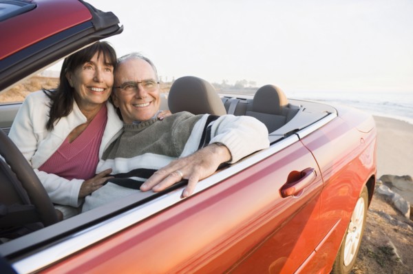 Older couple driving convertible on beach