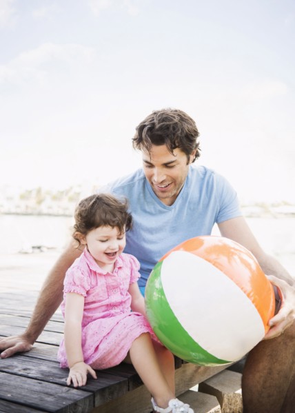 Caucasian father and baby daughter sitting on dock with beach ball