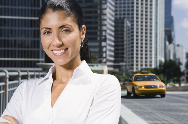 Smiling Mixed Race businesswoman near taxi in city
