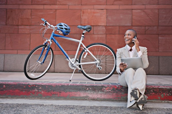 Businesswoman sitting on curb using digital tablet and cell phone