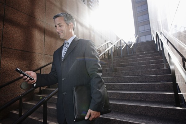 Hispanic businessman text messaging on steps