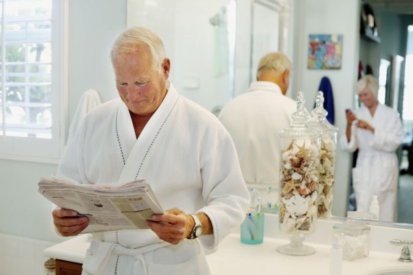 Caucasian man reading newspaper in bathroom