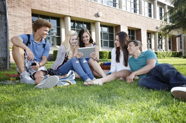 School friends hanging out on grass with digital tablet
