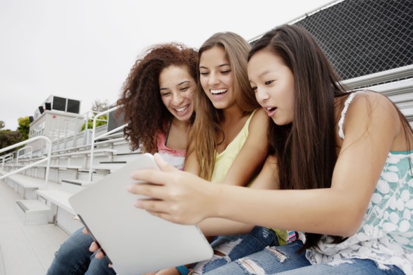 School friends sitting together on bleachers using digital tablet