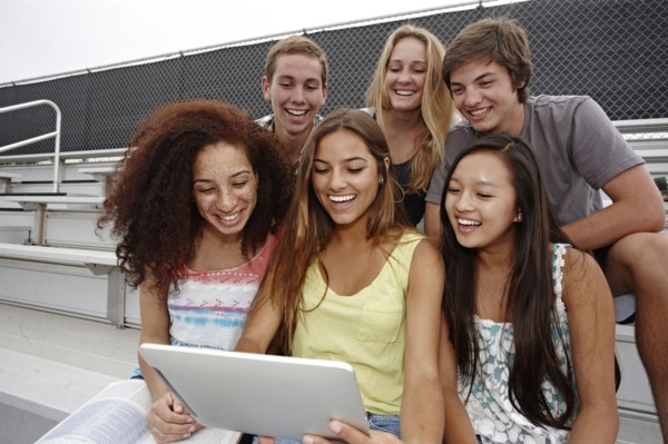 School friends sitting together on bleachers using digital tablet