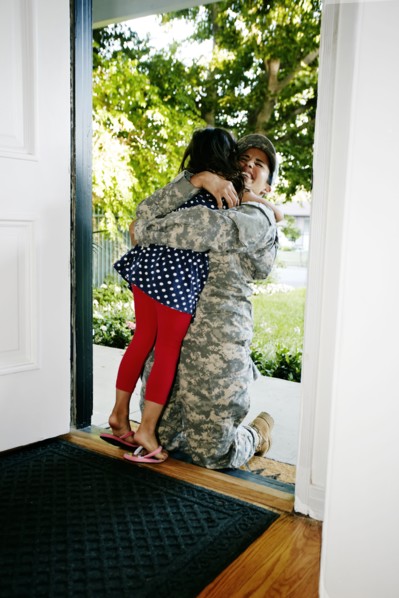 Mixed race soldier mother hugging daughter in front door