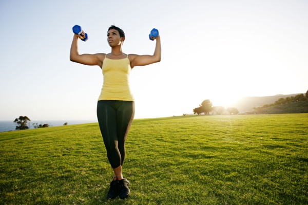 Black woman lifting weights in rural landscape