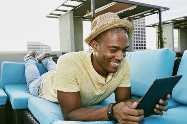Black man using digital tablet on sofa on urban rooftop