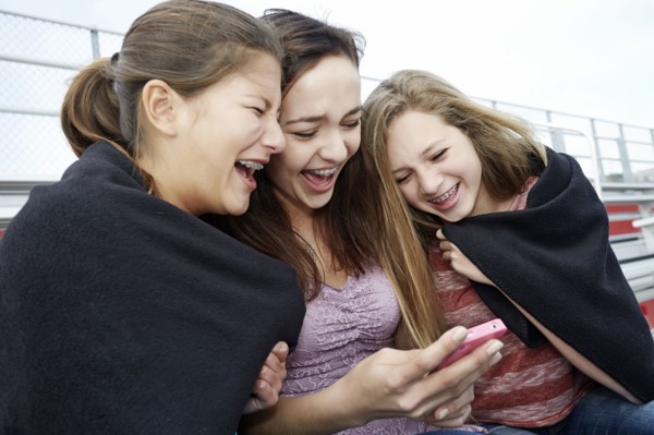 Teenage girls using cell phone in blanket