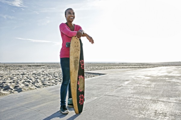 Older Black woman holding skateboard on beach