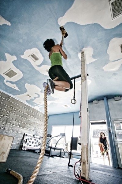 African American woman climbing rope in gym