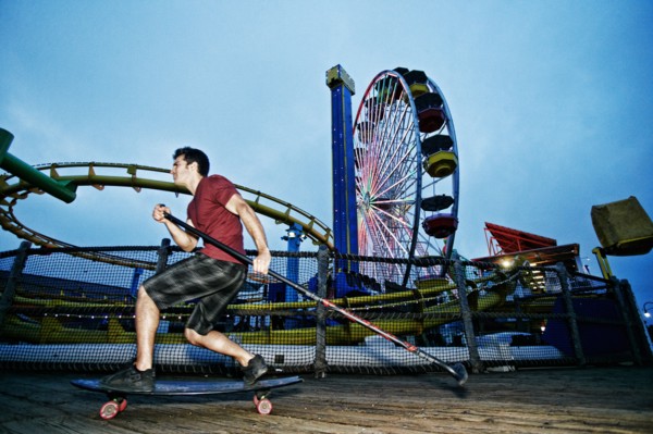Caucasian man skateboarding with paddle pole at amusement park