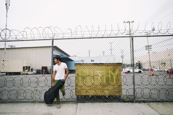 Mixed race musician leaning on fence holding guitar case