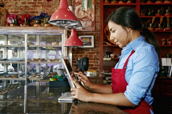 Hispanic cashier using digital tablet register in bakery