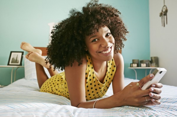 Smiling mixed race woman using cell phone on bed