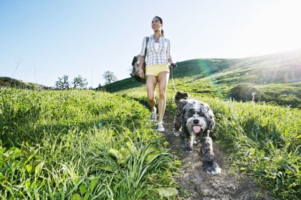 Mixed race woman walking dog on grassy hillside