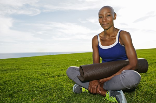 African American woman holding yoga mat in park