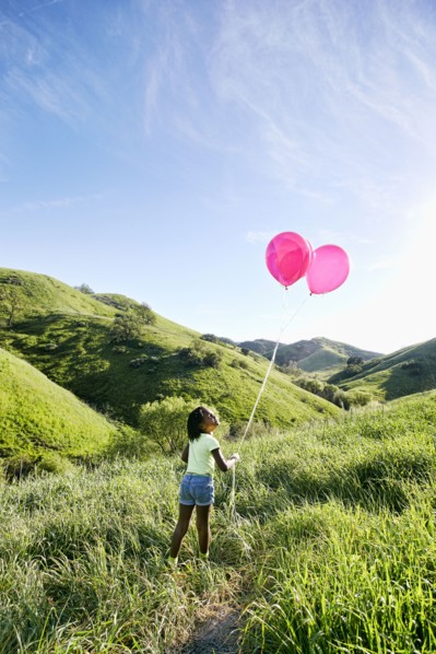 Black girl with balloons on rural hillside