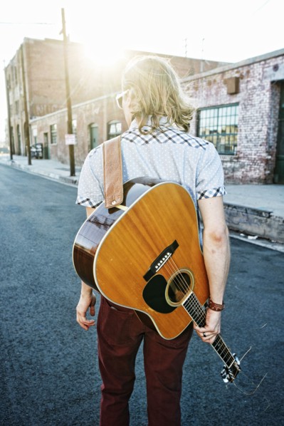 Caucasian man carrying guitar outdoors