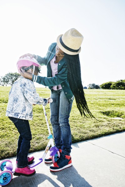 Black mother fastening helmet on daughter