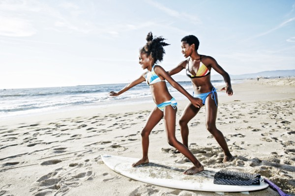 Black mother teaching daughter to surf on beach