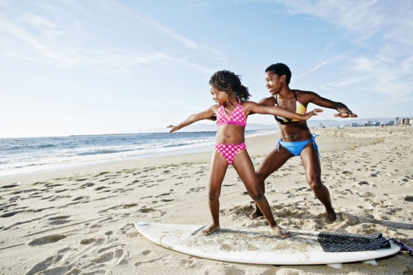 Black mother teaching daughter to surf on beach