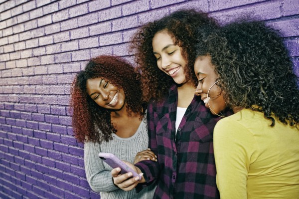 Women using cell phone outdoors at purple wall