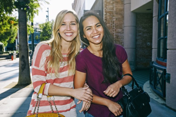 Women walking arm-in-arm on sidewalk