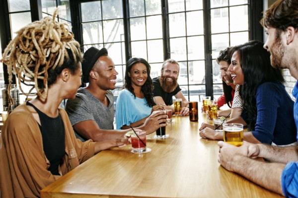 Smiling friends drinking at table in bar