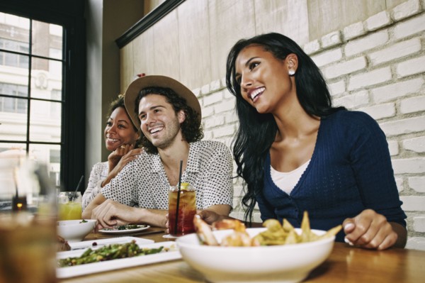 Smiling friends enjoying food and cocktails at table in bar