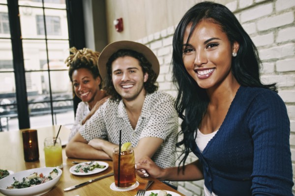 Smiling friends enjoying food and cocktails at table in bar