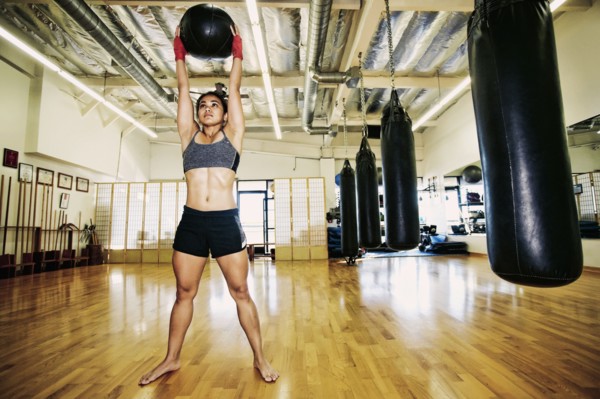 Asian woman lifting heavy ball in gymnasium