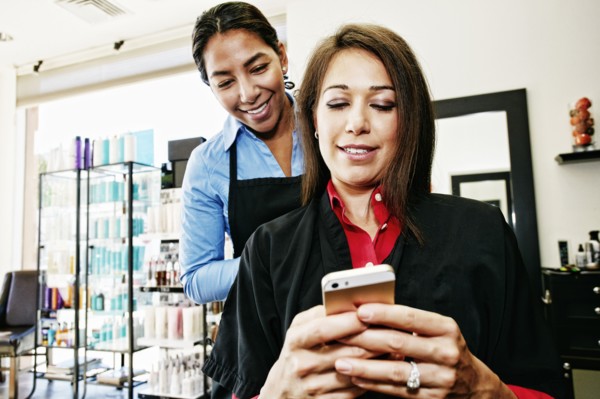 Hairdresser watching customer texting on cell phone in hair salon