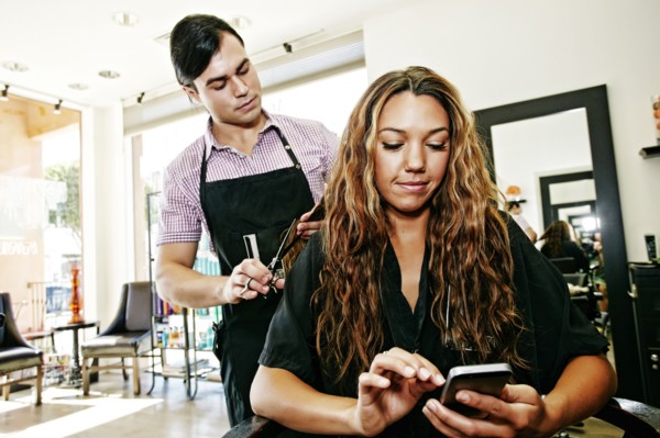 Hairdresser with customer texting on cell phone in hair salon