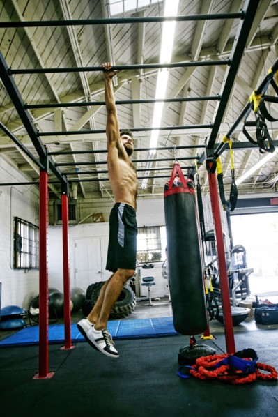 Mixed Race man hanging from bars in gymnasium