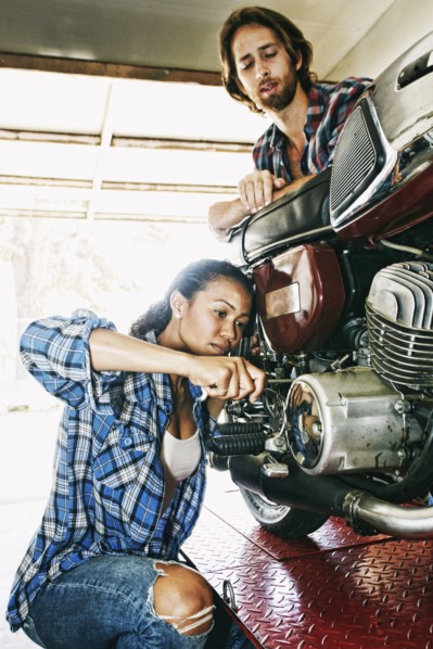 Man watching woman repairing motorcycle in garage