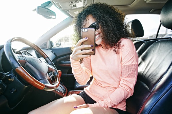 Smiling Hispanic woman in car posing for cell phone selfie
